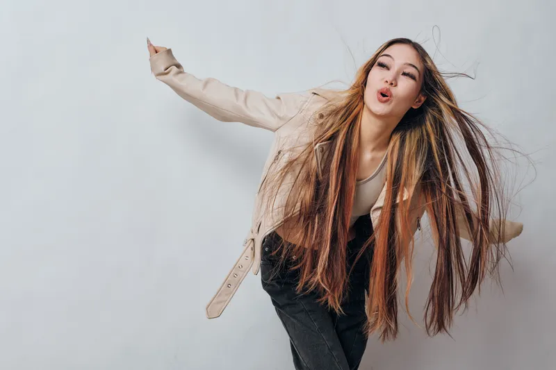 Young woman with long hair in casual clothes posing actively on grey background, expressing fun emotion and dynamic movement for lifestyle and fashion.