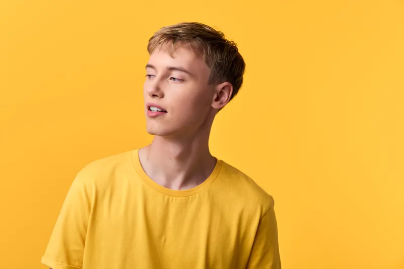 Young man in a bright yellow shirt against a solid yellow backdrop, looking away with a relaxed expression, casual fashion and lifestyle mood, studio style and vibrant color.