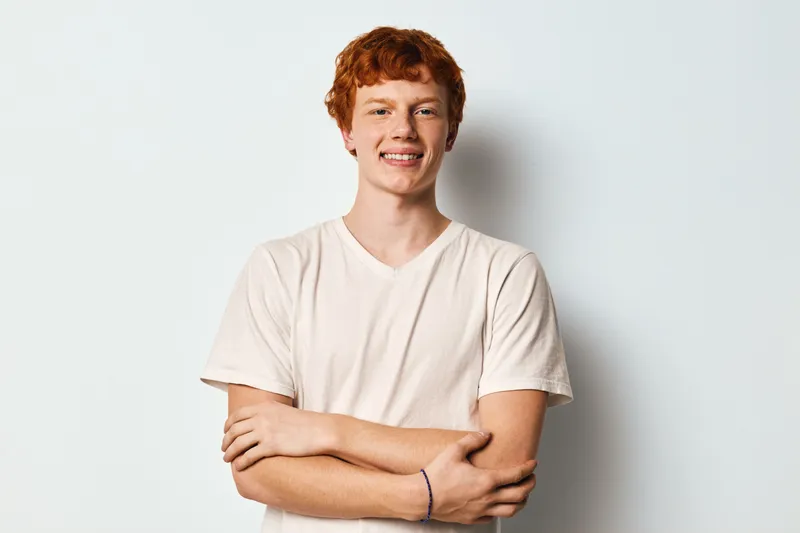Young man with red hair smiling front view against white background wearing casual t shirt with crossed arms expression for lifestyle portrait.