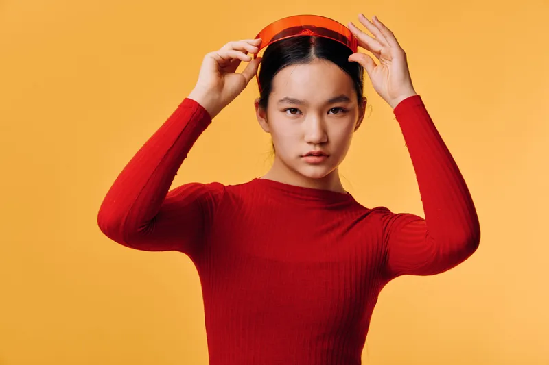 Young woman in red sweater holding red headphones on bright yellow background for lifestyle, fashion, technology, and casual modern portrait with serious expression and studio lighting.