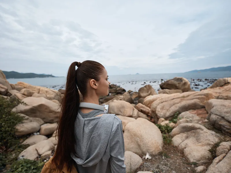Young woman with long hair in activewear enjoys a serene beach view, reflecting on nature while standing on rocky shore, promoting a healthy lifestyle