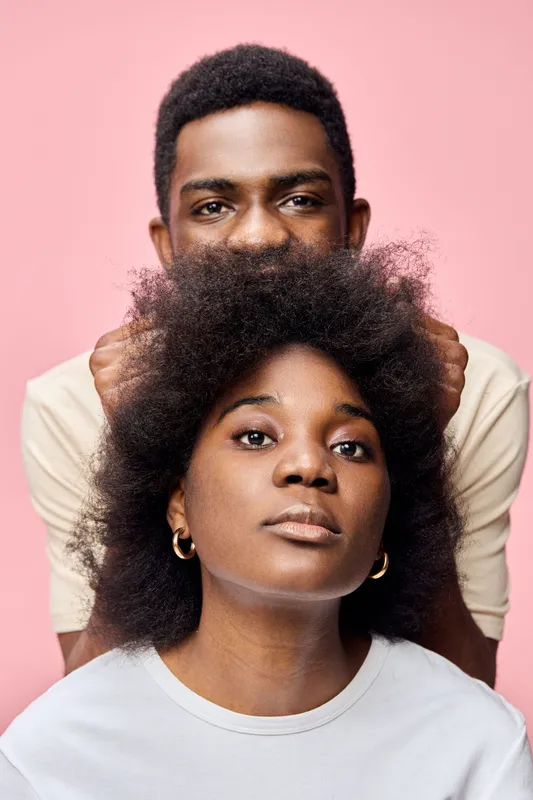 Portrait of a confident Black couple against a pink background, showcasing natural hair and stylish casual wear, expressing love and support