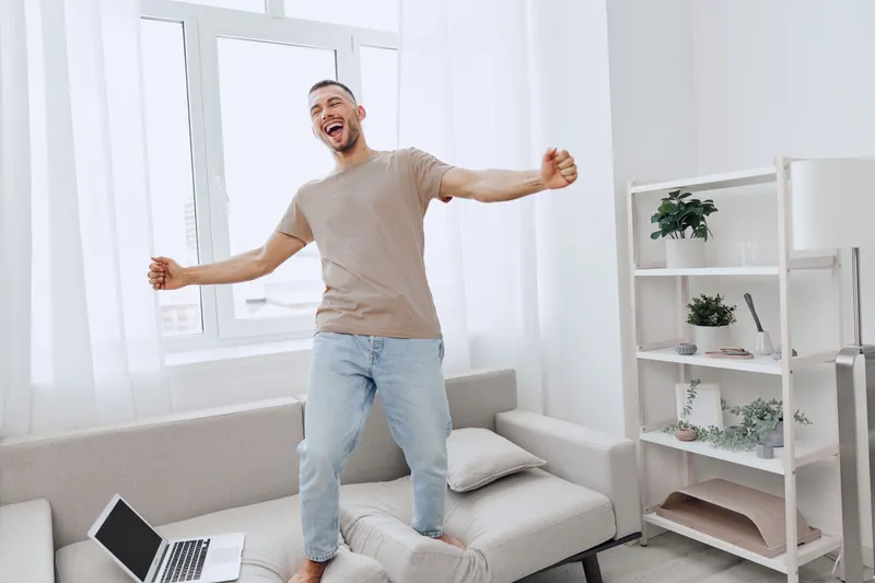 Energized man celebrating at home, embracing life and work balance, showcasing authentic expression and emotional freedom in a cozy, minimalistic setting.