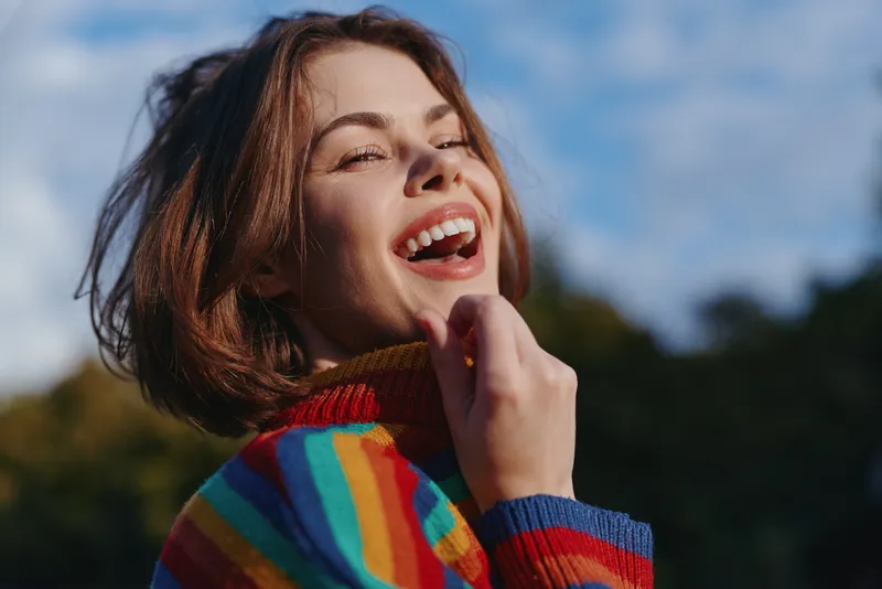 Young woman laughing outdoors, striped sweater and short hair bob, sunlight on freckled face, joyful lifestyle portrait in park for fashion, travel and carefree weekend vibes.