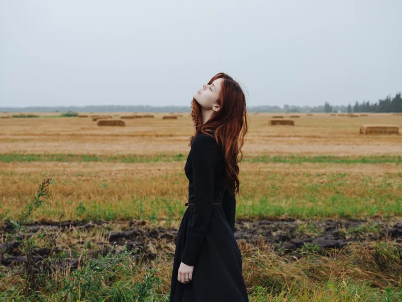 Красивая женщина в чёрном платье идёт по полю на природе осенью