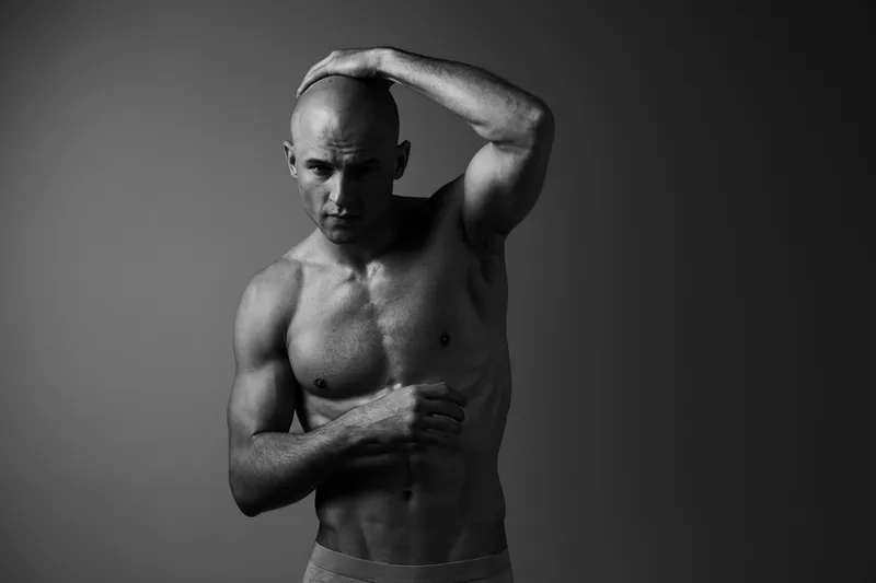 Black and white image of a strong man holding his head, showcasing a fit physique and intense expression, highlighting emotions and inner strength.