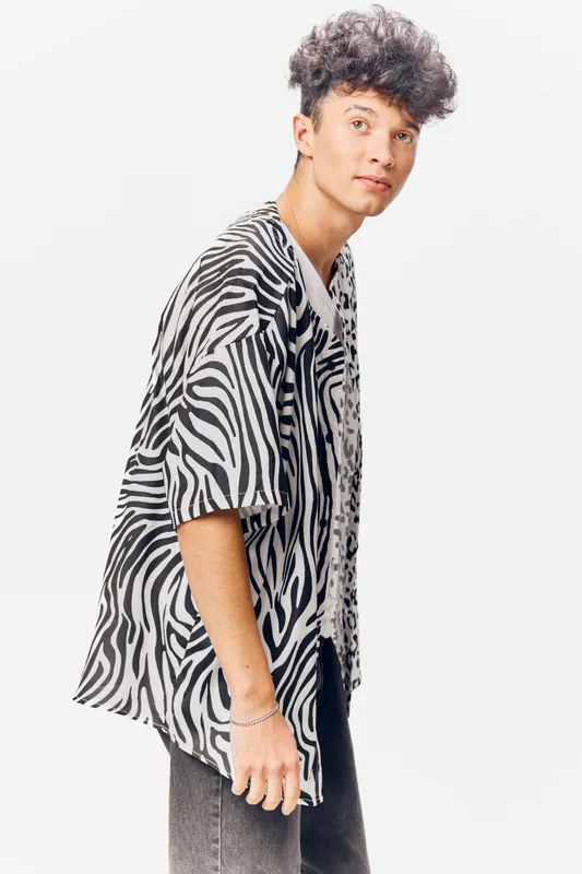 young man wearing zebra print shirt poses against white background with casual expression and natural curly hair, showcasing modern fashion style and urban vibe