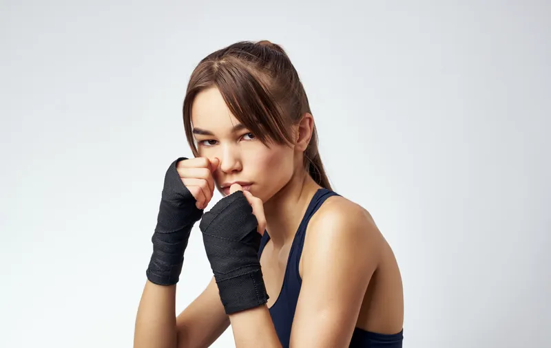 Женщина с гантелями в руках на светлом фоне, кадр обрезан, видна короткая футболка, фитнес