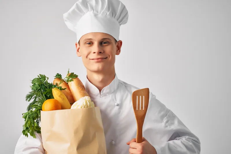 Весёлый шеф-повар мужского пола с упаковкой полезных продуктов питания, предоставляющий услуги на кухне