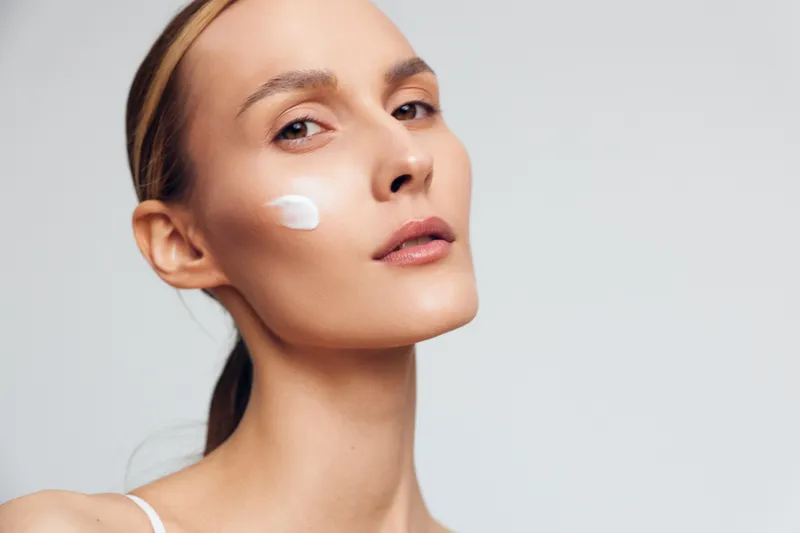 Woman applying face cream, closeup portrait in studio, skincare beauty and wellness routine on a light background, soft focus, smooth skin, calm self care, concept