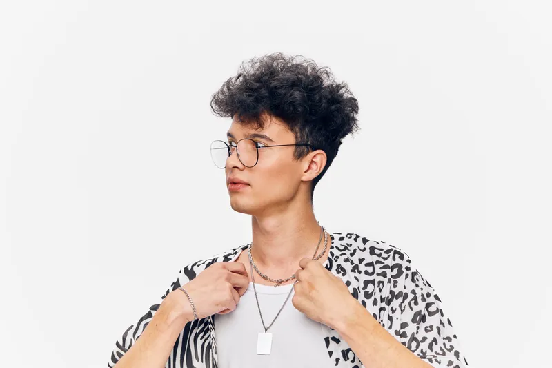 Young man with glasses wearing a patterned shirt, posing confidently against a white background, showcasing trendy fashion and modern style.