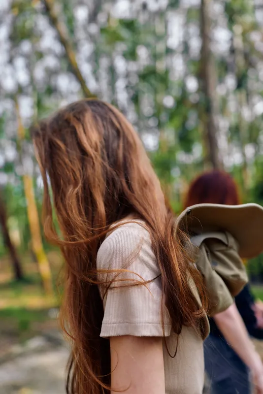 Woman with long hair in forest nature, casual backpack and walk with friend, side portrait and redhead profile in dappled daylight among trees and green woodland background.