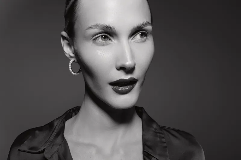 Portrait of a fair skinned Caucasian woman with slicked back hair and hoop earrings in dramatic black and white lighting.