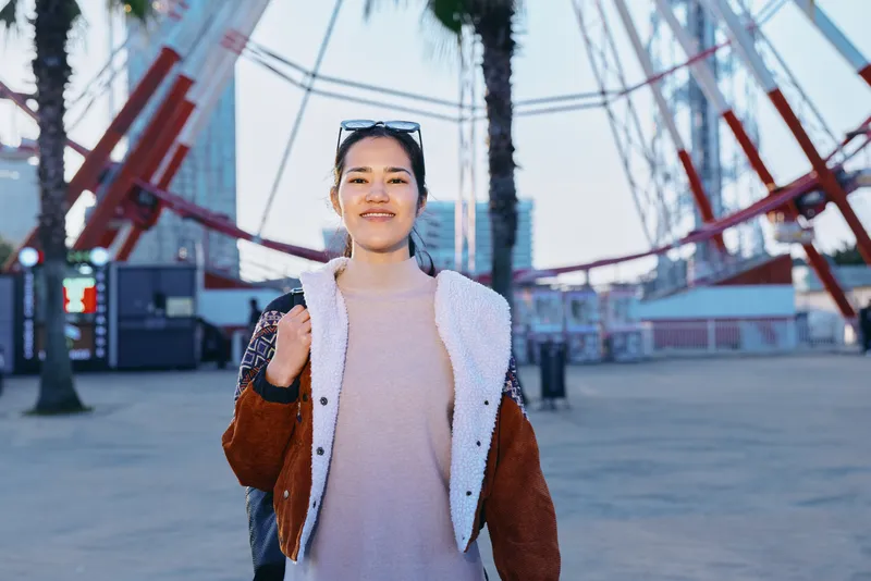 Woman in casual fashion outdoors on a boardwalk, palm trees and modern structures in the background, sunny day, confident pose, street style inspiration.