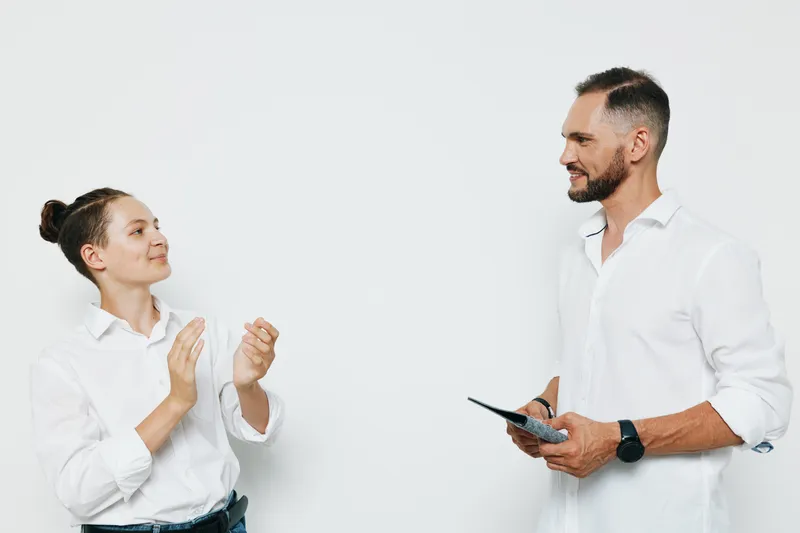 Two professionals stand against an isolated white background, exchanging ideas with a confident smile. A business man listens while a colleague gestures, portraying teamwork, leadership, and a