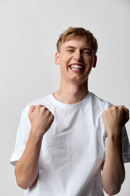 Joyful man with a fist pump, smiling in a casual tshirt, conveys celebration and happiness, showcasing energy and upbeat mood for marketing, social media, or ecommerce promotion in a bright studio