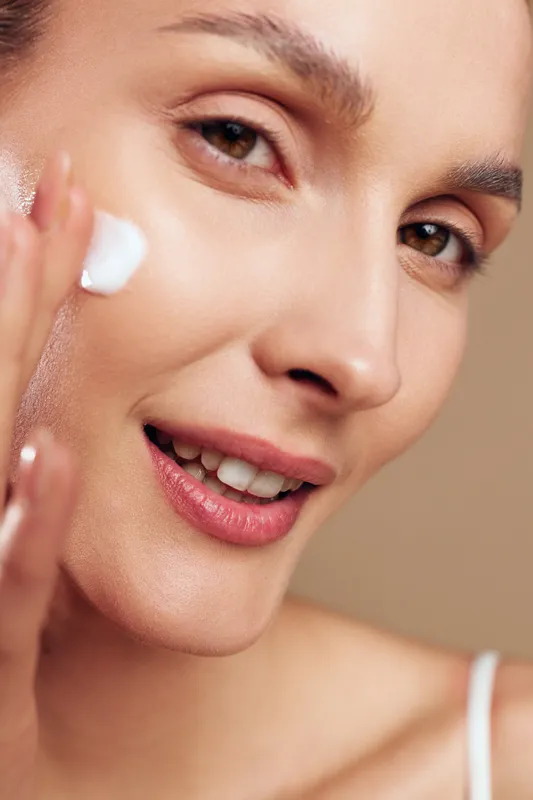 woman skincare face beauty closeup with serum and moisturizer, cream on cheeks and under eye, clean texture, soft light, natural makeup, healthy care, beige background, spa care, glowing skin