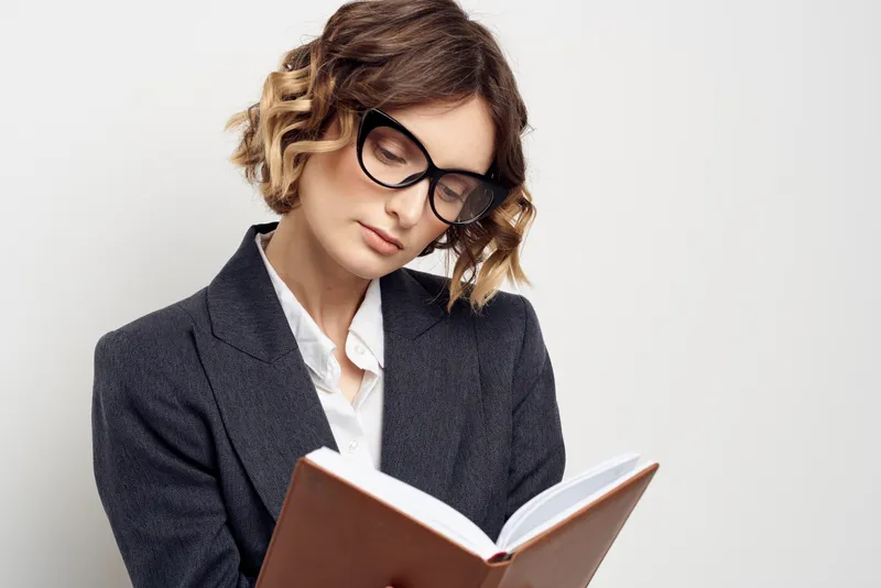 Деловая женщина в классическом костюме с блокнотом в руке и в очках на лице