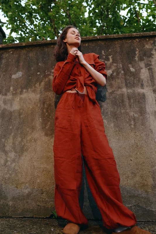 Woman lifestyle outdoors, confident pose, rust suit outfit, relaxed mood, soft breeze, sunlit backdrop, natural colors, greenery overhead