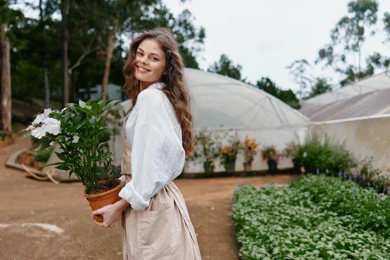Young woman holding a potted plant, smiling in a lush greenhouse environment, showcasing a connection to nature, beauty, and eco friendly living, perfect for healthy lifestyle themes