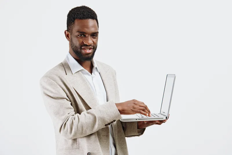 Professional confident man holding a laptop computer, wearing a beige blazer and white shirt, smiling and looking at camera, isolated on plain white background studio portrait. Business lifestyle conc