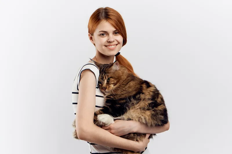 Рыжеволосая женщина держит в руке кота, полосатая футболка, светлый фон, дом, питомец