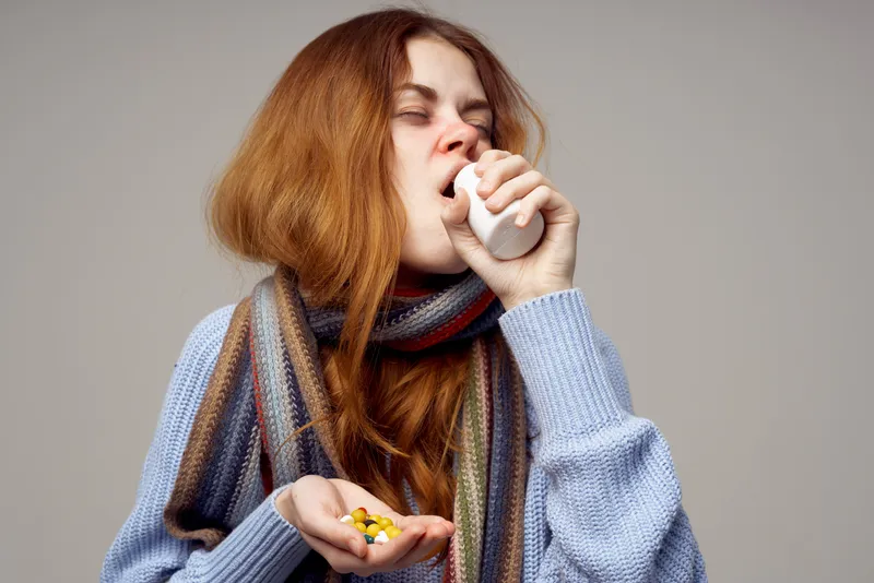 Женщина с банкой таблеток на сером фоне, на ней шарф