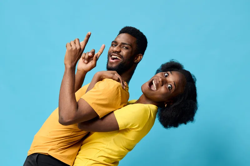 Happy young Black couple having fun together, posing against a blue background, showcasing joy and affection in colorful outfits