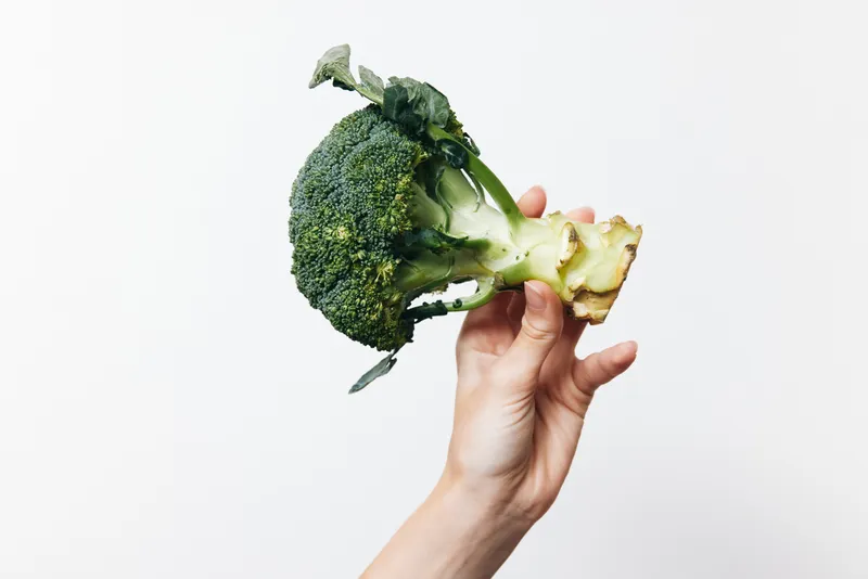 Свежая брокколи, которую человек держит на белом фоне