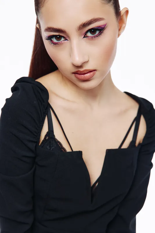 Close-up portrait of a young woman with dramatic makeup and sleek hair wearing black clothing showing fashion and beauty concept with creative mood on white background studio shot.