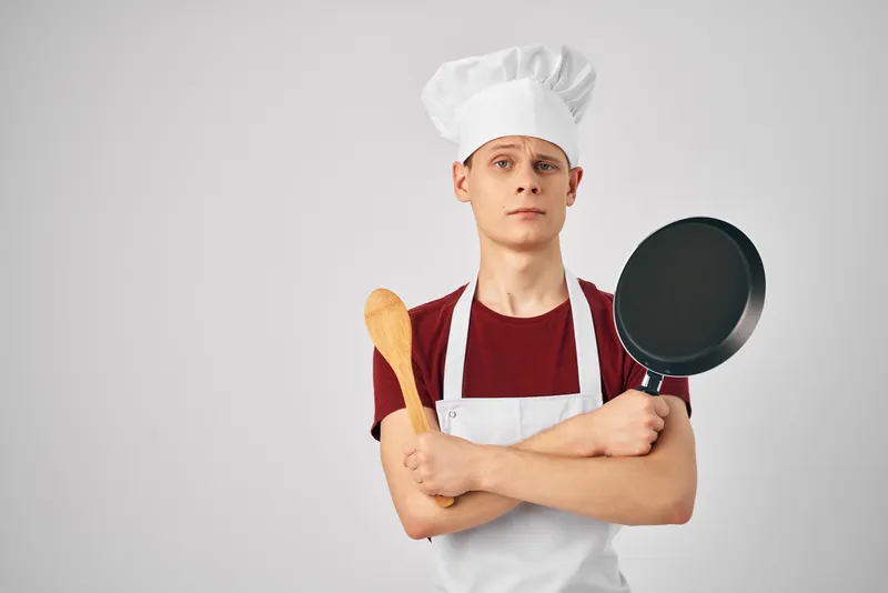 Повар-мужчина держит в руках сковороду на кухне, занимаясь профессиональным приготовлением пищи