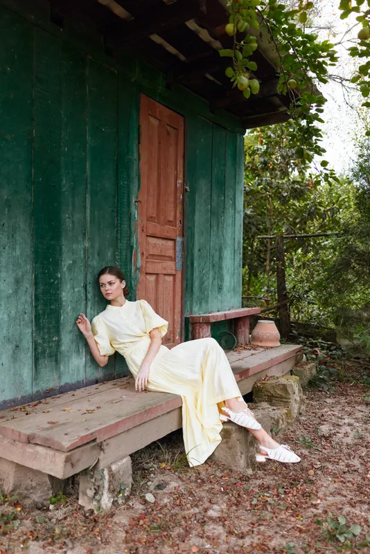 Woman in yellow dress leaning on rustic cottage bench outdoors with authenticity and inclusivity