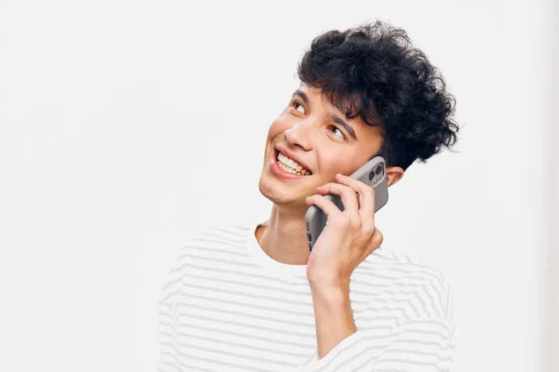 smiling man talking smartphone young adult casual striped shirt bright background communication and technology concept