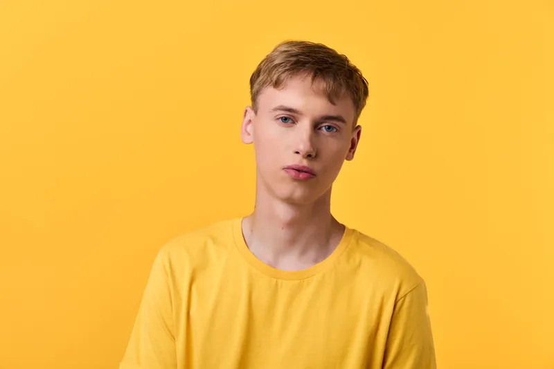 Young man wearing a yellow t shirt stands against a vibrant yellow backdrop, creating a bold monochrome fashion look ideal for studio, marketing imagery, fashion campaigns, or lifestyle shoots.