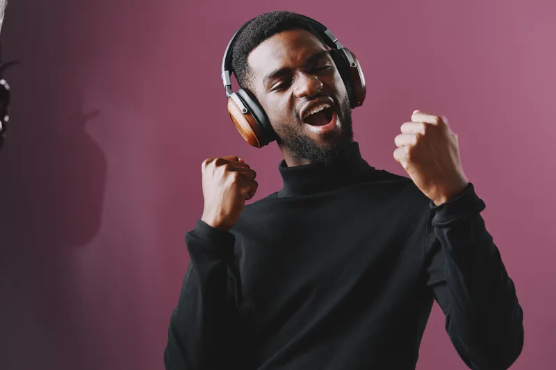 Excited Black man with headphones singing joyfully against a purple background, expressing passion for music and joyful emotions