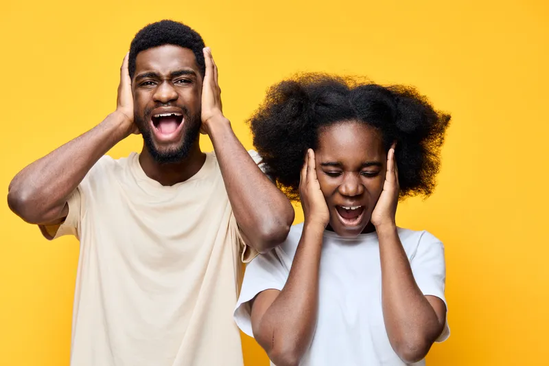 Young African American couple expressing frustration and stress with hands on ears against a bright yellow background, showcasing emotions and connection