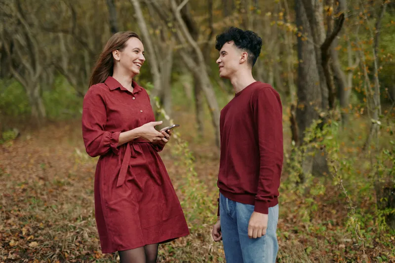 An authentic moment in autumn light shows a woman in a red dress conversing with a man in casual attire, conveying genuine emotion and a natural, believable interaction.