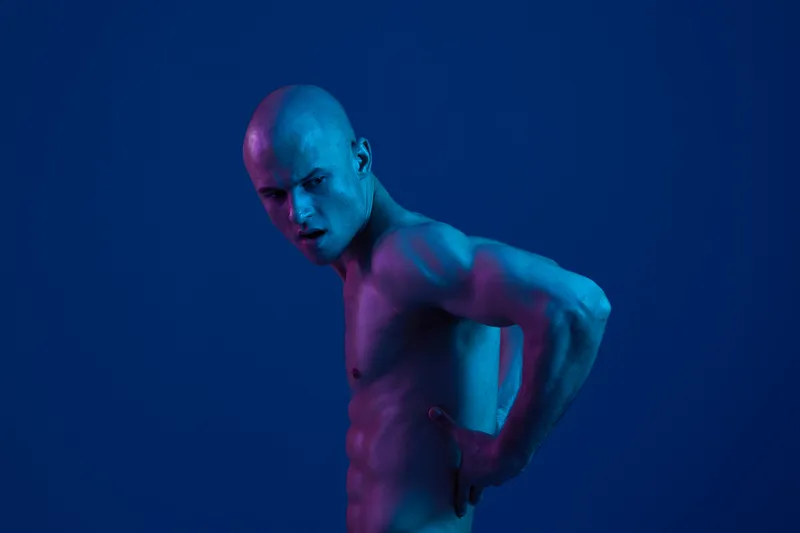 Male model posing against a vibrant blue background, showcasing a dynamic expression and athletic physique. Emphasizes light and shadows in artistic composition.