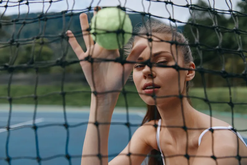 Young female tennis player focusing on a green tennis ball behind a net, showcasing intensity and determination in a vibrant outdoor setting