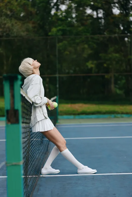 Young female tennis player in stylish sportswear enjoying a moment of relaxation on the court, showcasing a vibrant and seasonal outdoor atmosphere