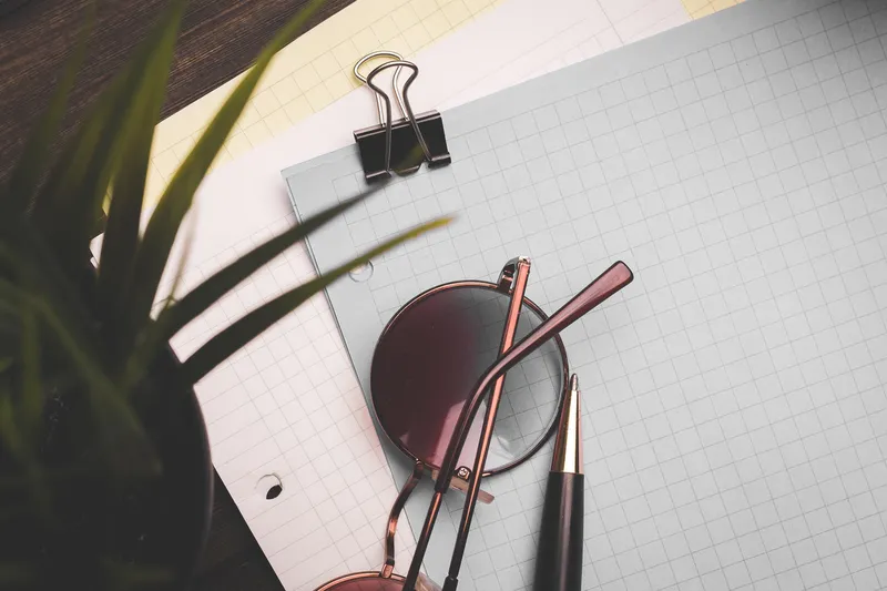 Канцелярские принадлежности: блокноты, очки, бумага со скрепкой, чашка кофе и цветок