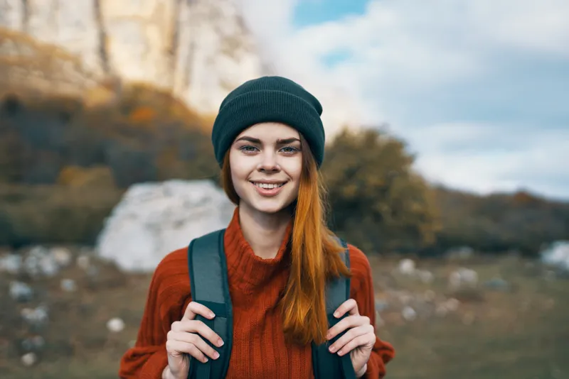 Симпатичная женщина-туристка в кепке наслаждается отдыхом на открытом воздухе на фоне горного пейзажа
