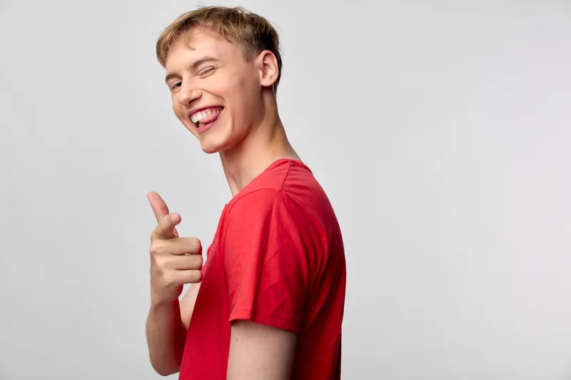 Smiling man in a redshirt pointing in a casual studio setting, conveying happiness, friendly energy, clear gesture and confident pose for promotional, lifestyle or product related usage in modern