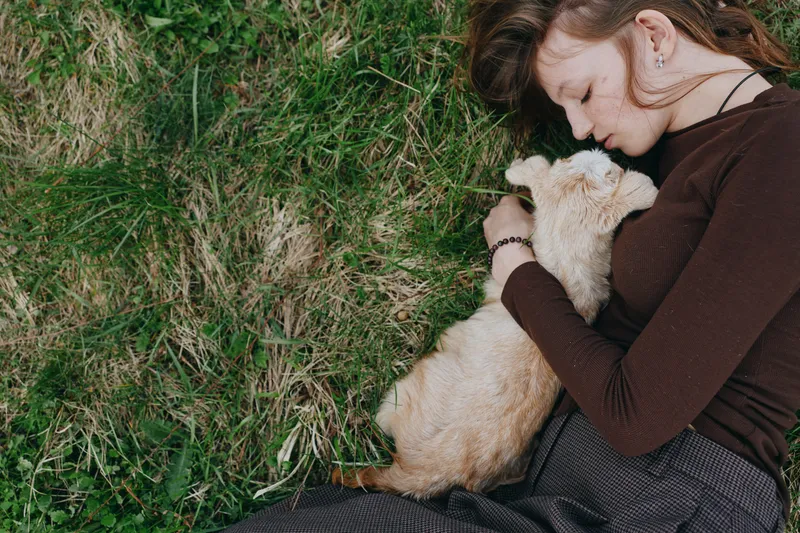 Young woman lying on the grass gently hugging a baby goat with closed eyes in a peaceful outdoor lifestyle moment during spring.