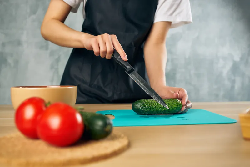 Женщина в черном фартуке на кухне нарезает овощи для салата, придерживаясь диеты