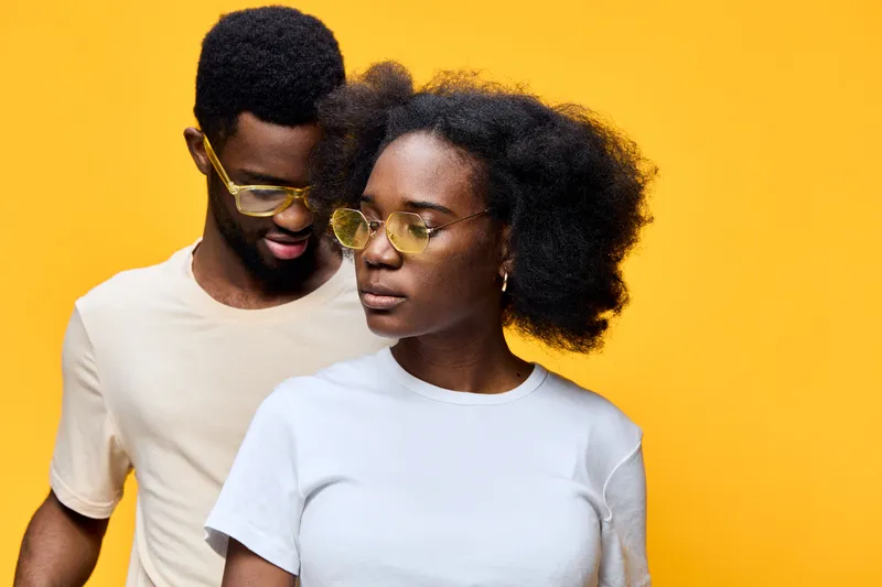 Stylish African couple posing with yellow sunglasses against a bright yellow background, showcasing a trendy summer vibe, fashionable attire, and vibrant emotions