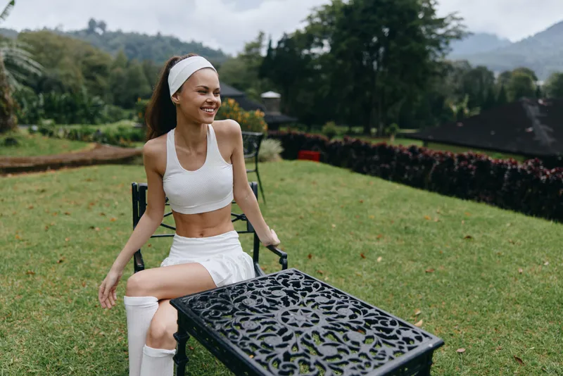 Joyful fitness model in activewear sitting on a chair outdoors, radiating health and positivity in a lush green environment