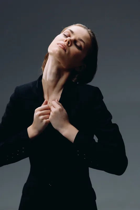 Elegant woman in black jacket posing with closed eyes and relaxed expression in studio setting