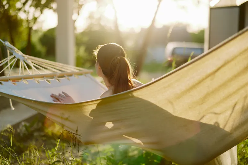 Relaxing woman in a hammock during golden hour, enjoying nature and tranquility in a sunlit garden Natural beauty, warmth, and peaceful emotion