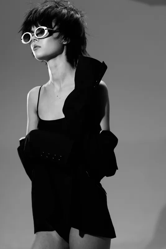 Stylish woman wearing sunglasses and black dress in a studio, black and white fashion portrait with confident expression and modern vibe.